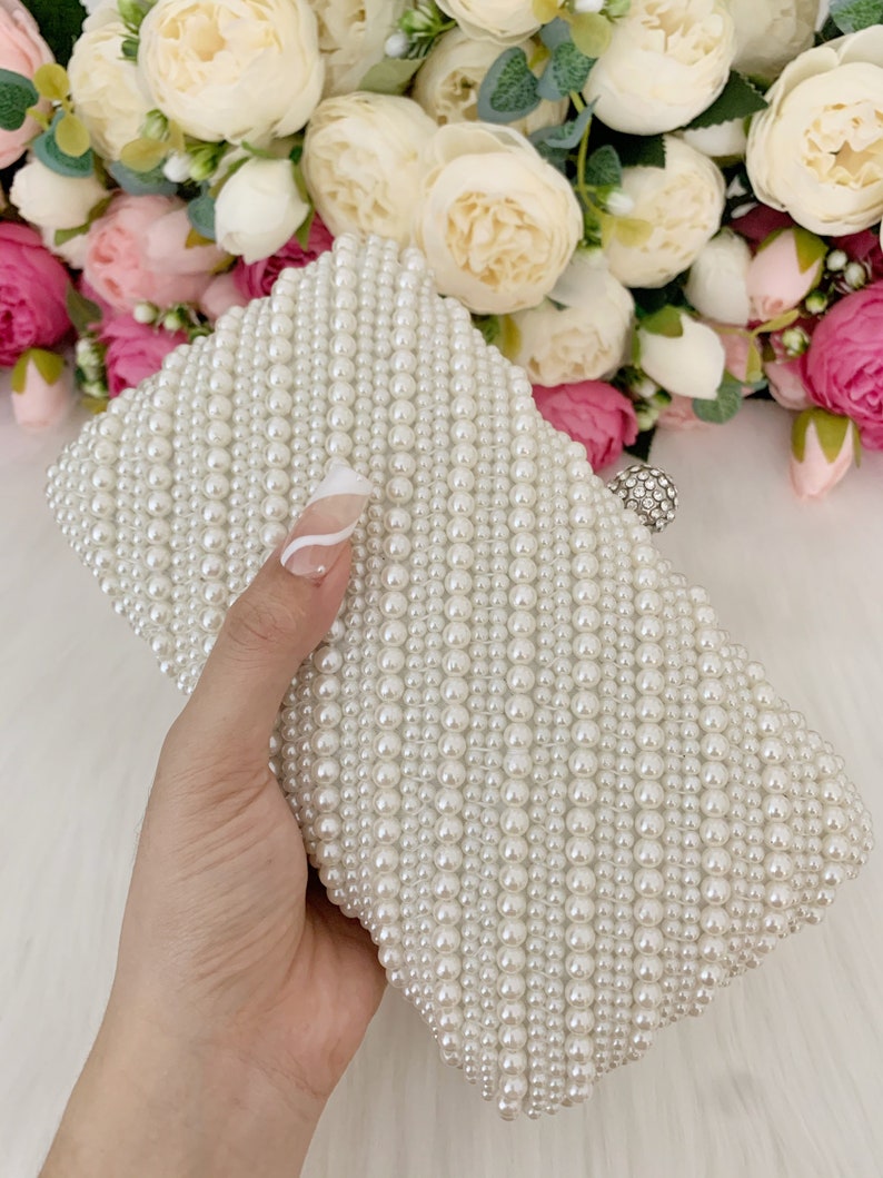 Peut inclure: Une pochette blanche en perles avec un fermoir argent&eacute;. La pochette est faite de petites perles rondes cousues ensemble en forme de losange.