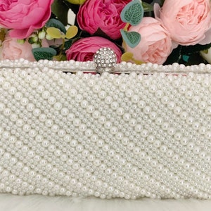 Peut inclure: Une pochette blanche recouverte de fausses perles avec un fermoir en strass transparent.