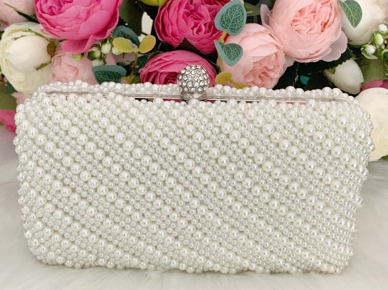 Peut inclure: Une pochette blanche recouverte de fausses perles avec un fermoir en strass transparent.
