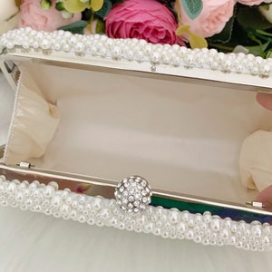 Peut inclure: Une pochette blanche orn&eacute;e de perles et d'un fermoir en strass transparent.