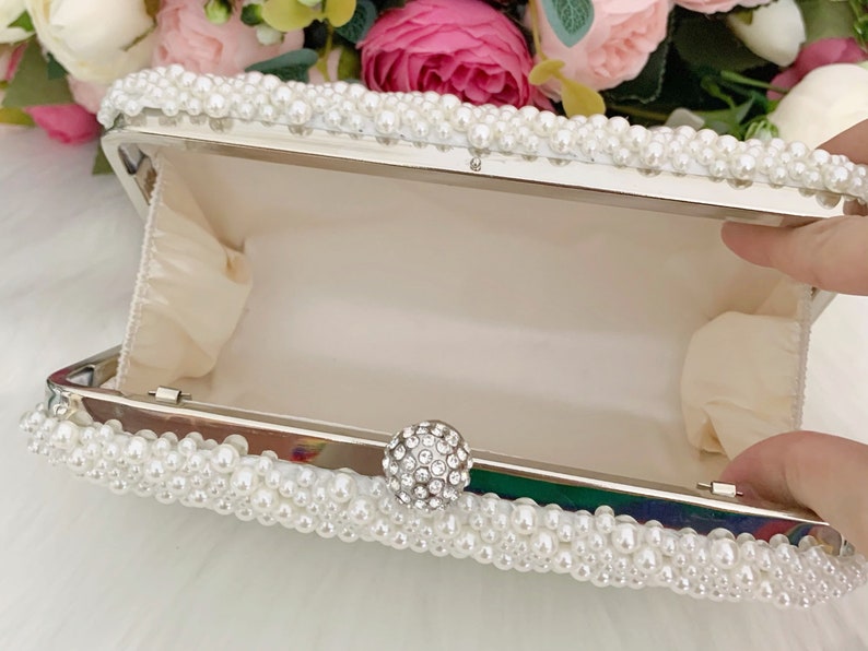 Peut inclure: Une pochette blanche orn&eacute;e de perles et d'un fermoir en strass transparent.