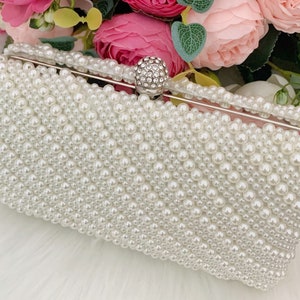 Peut inclure: Une pochette blanche recouverte de fausses perles avec un fermoir en cristal transparent.