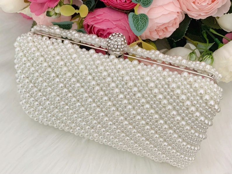 Peut inclure: Une pochette blanche recouverte de fausses perles avec un fermoir en cristal transparent.
