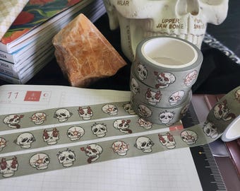 Op de afbeelding: Vier rollen washi tape met een groene achtergrond en een wit schedelontwerp. De schedels hebben rode vlammen en tongen. De tape bevindt zich op een wit geruit oppervlak.