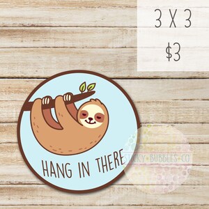 May include: A round sticker with a cartoon sloth hanging upside down from a branch. The sloth is brown with a light brown face and closed eyes. The background is light blue with the text "HANG IN THERE" in brown letters.