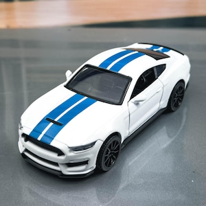 May include: A white toy car with blue racing stripes running down the center. The car has black wheels and a black interior. The car is a miniature replica of a sports car.