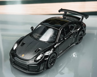May include: A black model car with a rear spoiler. The miniature vehicle has detailed features, including headlights and wheels. The car is displayed on a reflective surface. The model is a miniature replica.
