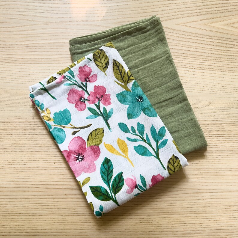 May include: Two fabric cloths, one with a floral pattern in pink, green, and blue on a white background, and the other a solid green color.