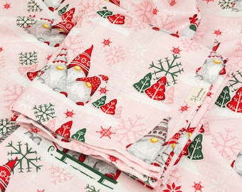 May include: Pink fabric with a white snowflake and red and green Christmas tree pattern. The fabric features a repeated pattern of gnomes with red hats and white beards. The fabric is folded in a stack and has a small white tag with the text "Handmade Creations" on it.