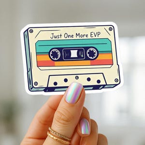 May include: A sticker featuring a retro cassette tape design with the text "Just One More EVP." The cassette has a teal, orange, and yellow striped design. The sticker is held by a hand with iridescent nails and gold rings.