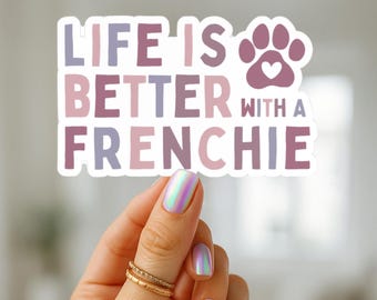 May include: A sticker with the text "LIFE IS BETTER WITH A FRENCHIE" in shades of purple and pink, with a paw print graphic. The sticker is held by a hand with iridescent nail polish and gold rings.