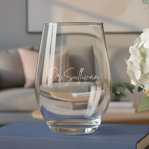 May include: A white ceramic mug with a black handle and the text "But First, Coffee" in a black, bold font. The mug is sitting on a wooden surface. The mug is 4 inches tall.