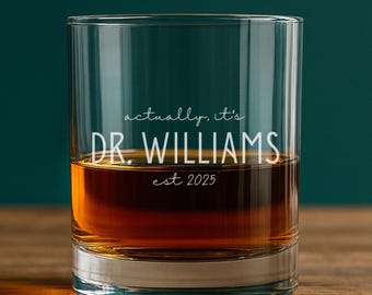 Puede incluir: Un vaso de cristal transparente lleno de un líquido de color ámbar. El vaso presenta un texto impreso en blanco que dice "actually, it's DR. WILLIAMS est 2025". El vaso tiene una base gruesa y sólida con paredes laterales rectas.
