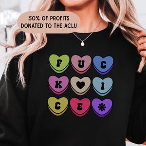 May include: Black sweatshirt with a colorful heart design. Each heart has a letter or symbol: F, U, C, K, a heart, I, C, E, and a star. The text "50% of profits donated to the ACLU" is at the top.