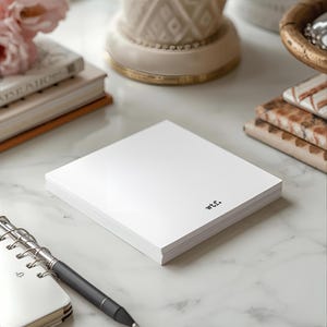 May include: A stack of white notepaper with the text "wtf." printed in black. The notepad is on a white marble surface, with a pen, a small notebook, and decorative items in the background.