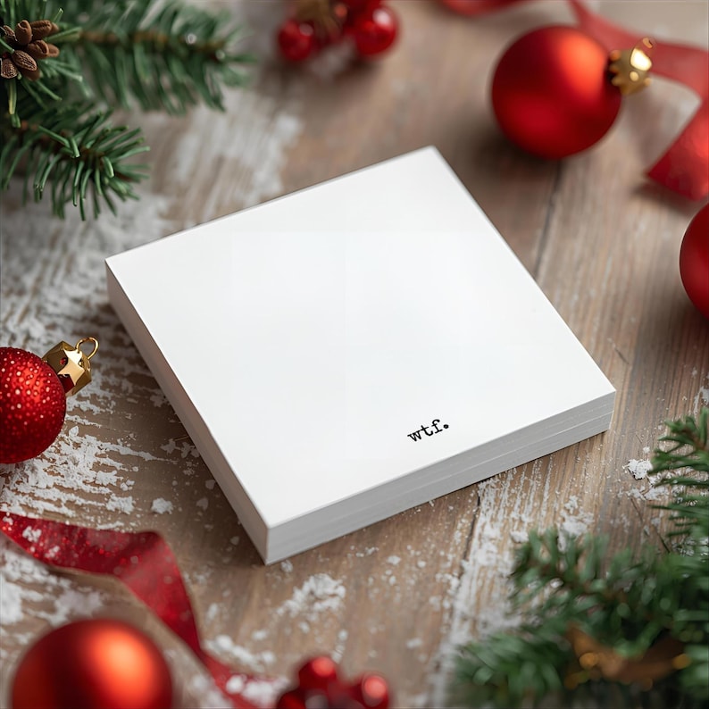 May include: A stack of white notepaper with the word "wtf." printed in black. The notepaper is surrounded by Christmas decorations, including red ornaments, pine branches, and red ribbon.