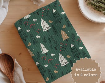 May include: A folded green kitchen towel with a repeating pattern of stylized Christmas trees, birds, and berries. The towel has a ribbed texture and the text "Available in 4 colors" is visible.