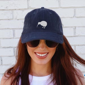May include: Navy blue corduroy baseball cap with a white kiwi bird design. The cap has a curved brim and a classic six-panel construction. The kiwi bird is embroidered on the front of the cap.