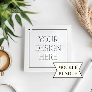 May include: A square white card with the text "YOUR DESIGN HERE" inside a black border. A banner below reads "MOCKUP BUNDLE". The image includes a coffee cup, pen, and greenery, suggesting a design or stationery mockup.