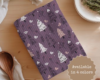 May include: A folded purple fabric with a repeating pattern of white and tan trees, birds, and sprigs. The text "Available in 4 colors" is in a brown starburst shape. The fabric is on a wooden surface.