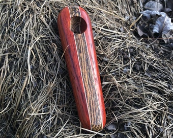 May include: A wooden pipe with a red and brown striped design. The pipe has a round hole in the center.