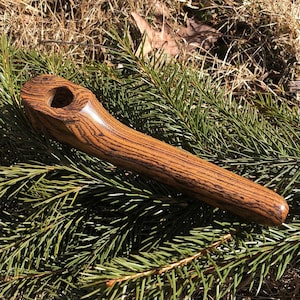 Op de afbeelding: Een gepolijste houten rookpijp met een opvallend donkerbruin nerfpatroon over het gehele langwerpige, gebogen lichaam. De pijp heeft een gladde, afgeronde afwerking en een ronde komopening aan het bredere uiteinde, met natuurlijke houttexturen.