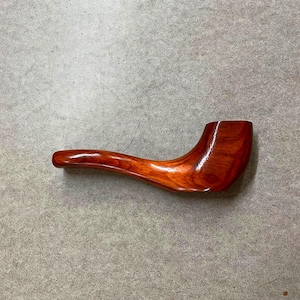 May include: A handcrafted, wooden pipe with a rich, reddish-brown finish. The pipe features a curved stem and a bowl, showcasing the natural wood grain. The smooth, polished surface suggests a well-made smoking accessory.