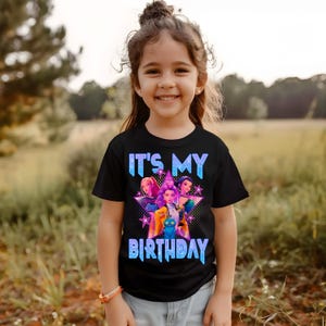 May include: A black t-shirt with the text "IT'S MY BIRTHDAY" in blue and a graphic of three cartoon characters inside a star. The shirt is worn by a young girl smiling in front of a blurred outdoor background.