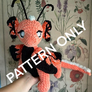 May include: A handmade plush creature with a peach-colored body, black and orange wings, and large, expressive eyes. The plush has a fluffy texture and a long tail. The text "PATTERN ONLY" is visible on the image.