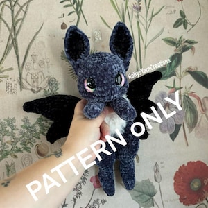 Puede incluir: Un juguete de peluche de murciélago tejido a crochet con alas negras y un cuerpo azul. El murciélago tiene ojos grandes y brillantes y una barriga blanca. El texto "PATTERN ONLY" está superpuesto en la imagen.
