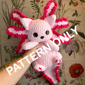 May include: Pink crocheted axolotl plush toy with pink and white ruffled edges. The toy is being held by a hand. The text "PATTERN ONLY" is superimposed on the image.
