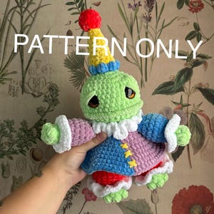 May include: A crocheted doll in the form of a whimsical character. The doll is mainly green, with a yellow and blue hat, a pink and blue outfit, and red accents. The text "PATTERN ONLY" is displayed across the top.
