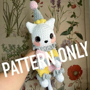 Puede incluir: Patrón de crochet para un lindo gato blanco que lleva un disfraz a rayas de colores. El gato tiene mejillas rosadas y ojos grandes y negros. El patrón está disponible para descargar.