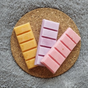 Puede incluir: Tres fundentes de cera, uno amarillo, uno rosa y uno morado, sobre un fondo de corcho.