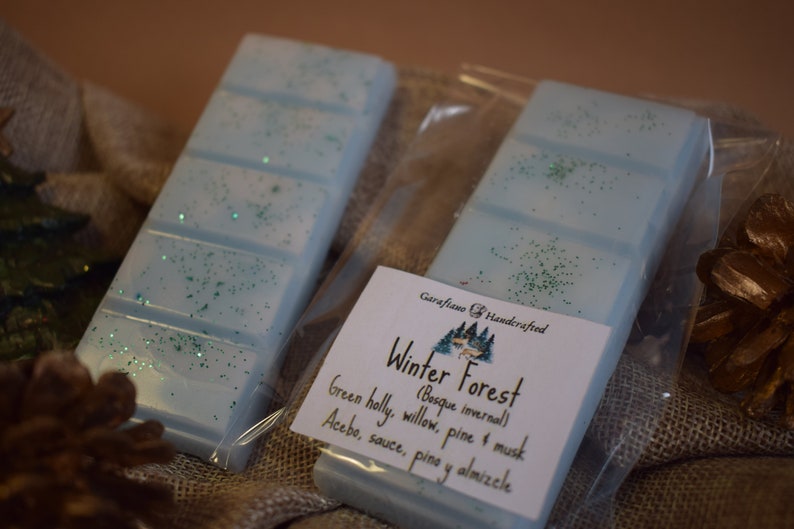 May include: Two light blue wax melt bars with green glitter accents, packaged in clear plastic. A label reads "Winter Forest" with scent notes. The bars are displayed on a burlap surface, suggesting a natural theme.