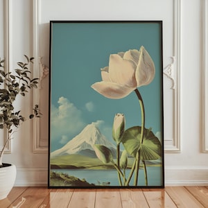 May include: A framed art print featuring a large, light pink lotus flower with green leaves and buds against a blue sky. A snow-capped mountain and lake are in the background. The artwork is in a black frame.