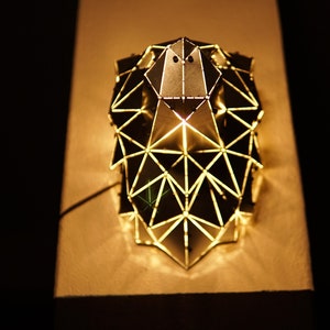 May include: A geometric metal lampshade with a triangular design. The lampshade is lit from within, casting a warm glow.