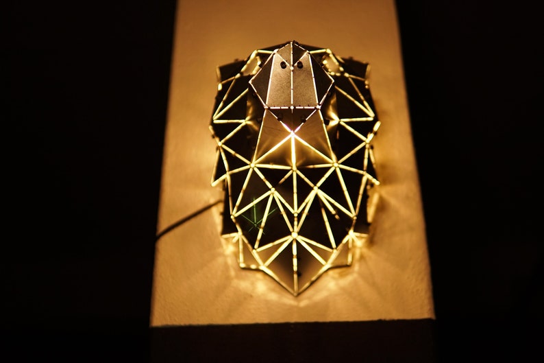 May include: A geometric metal lampshade with a triangular design. The lampshade is lit from within, casting a warm glow.