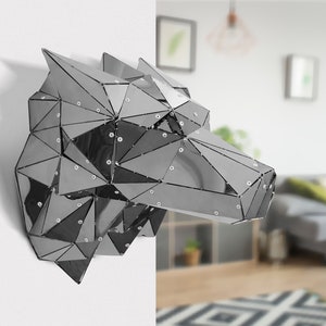 May include: A silver geometric wolf head sculpture made of reflective metal panels. The sculpture is mounted on a white wall.