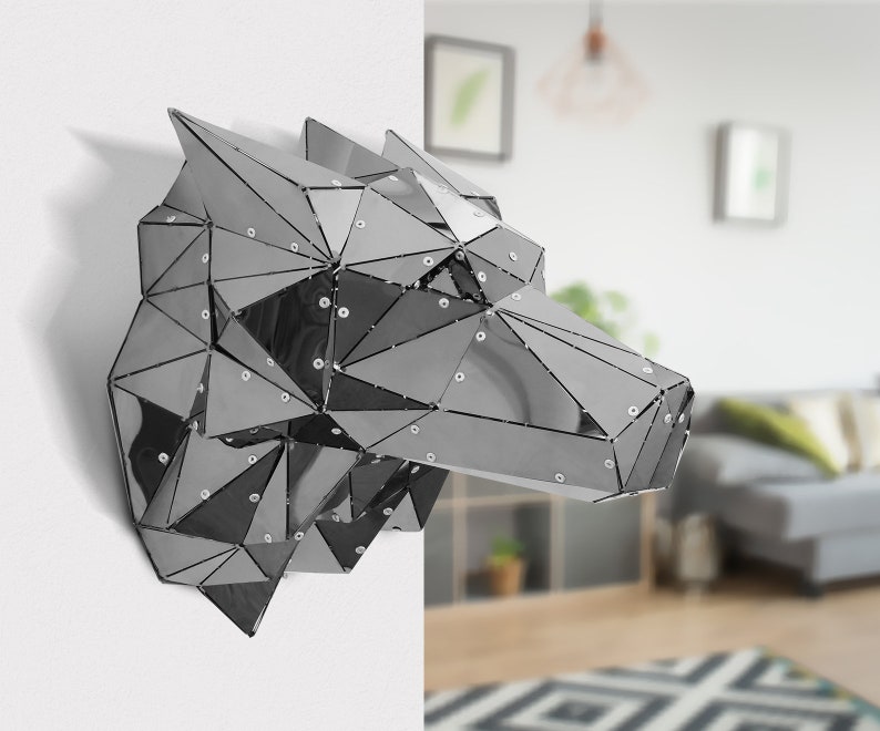 May include: A silver geometric wolf head sculpture made of reflective metal panels. The sculpture is mounted on a white wall.