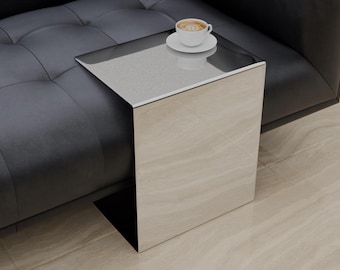 May include: A silver metal side table with a square top and a curved edge. A white ceramic coffee cup with a brown liquid sits on the table.