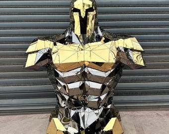 May include: A metallic sculpture of a Spartan warrior bust. The sculpture features a gold helmet with a red plume, gold chest and shoulders, and a silver torso. The design is geometric and angular, with a reflective surface.