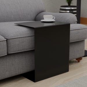 May include: A black side table with a rectangular top and a long, narrow base. The table is positioned next to a gray sofa.