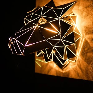 May include: A geometric wolf head wall sculpture made of metal with a warm, glowing light emanating from within.