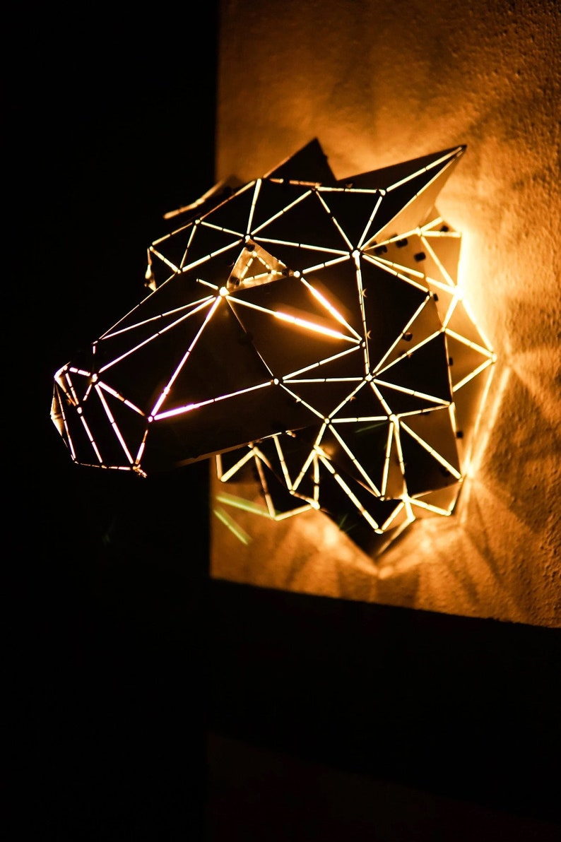 May include: A geometric wolf head wall sculpture made of metal with a warm, glowing light emanating from within.