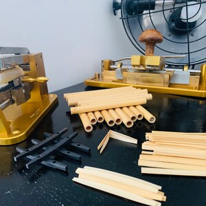 May include: Two gold-coloured metal tools for making bamboo flutes, with a pile of cut bamboo pieces and a few assembled flutes.