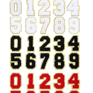 May include: Three sets of iron-on numbers, 0-9, in white with gold trim, black with gold trim, and red with gold trim. The numbers are in a block font style and are arranged in three rows.