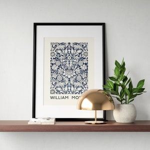 May include: A framed print of a blue and white floral pattern with the text "WILLIAM MORRIS" at the bottom. A gold dome lamp and a potted green plant are on a brown shelf.