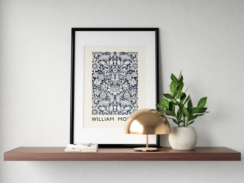 May include: A framed print of a blue and white floral pattern with the text "WILLIAM MORRIS" at the bottom. A gold dome lamp and a potted green plant are on a brown shelf.