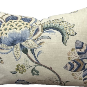 Puede incluir: Una almohada decorativa con un patr&oacute;n floral en tonos azules, verdes y marrones sobre un fondo crema.